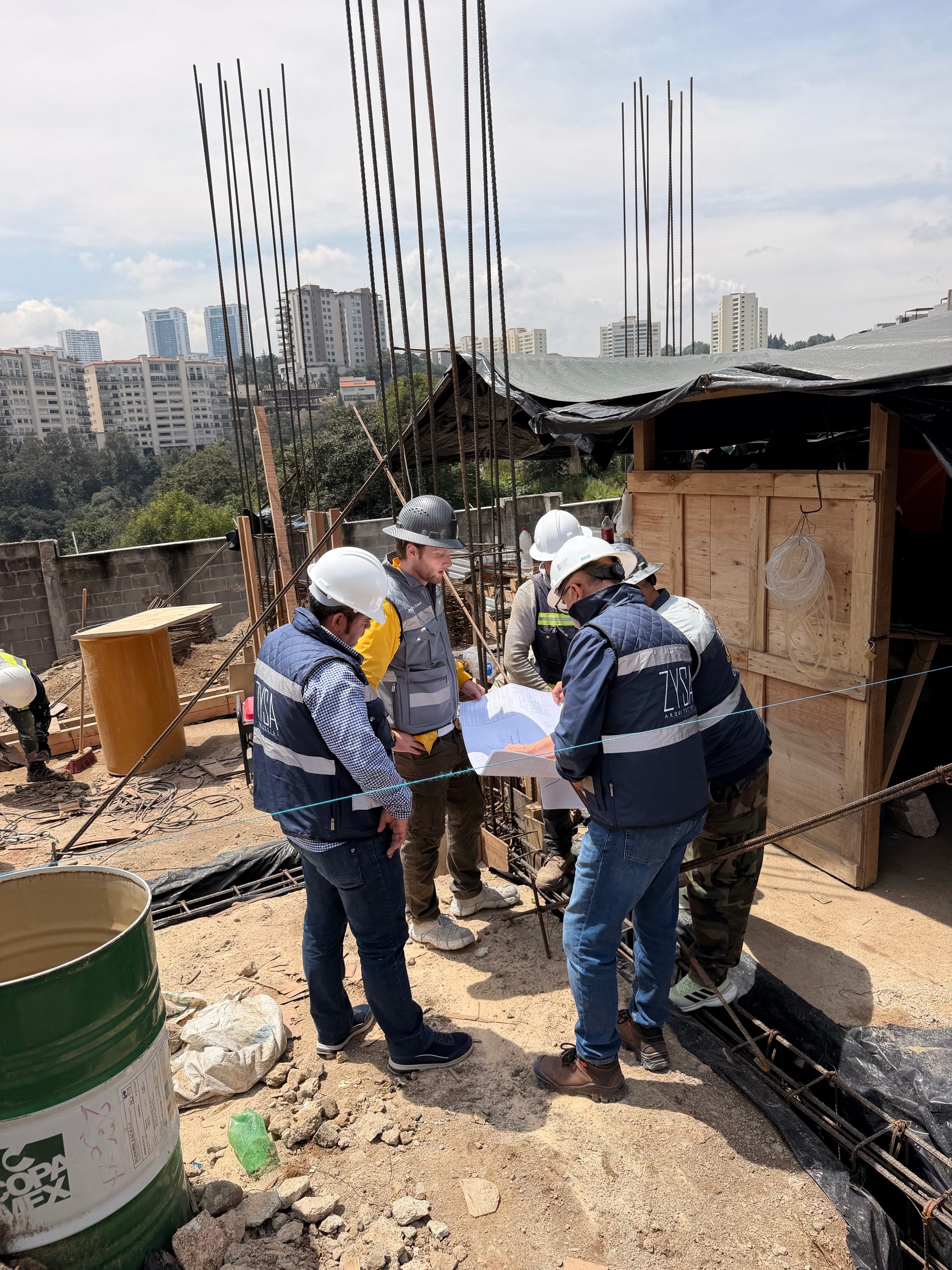 Equipo de ZYSA con cascos y chalecos revisando planos durante una visita de obra