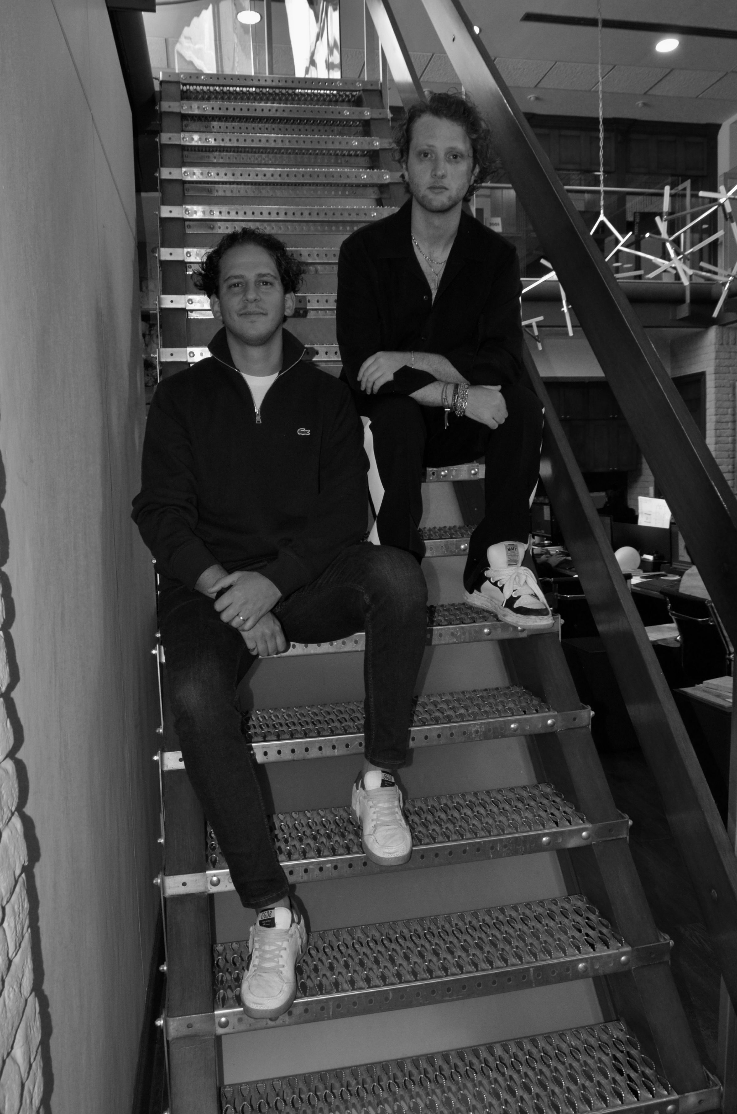 Anthony Salame y Eric Zyman, socios fundadores de ZYSA, sentados en una escalera metálica, en blanco y negro