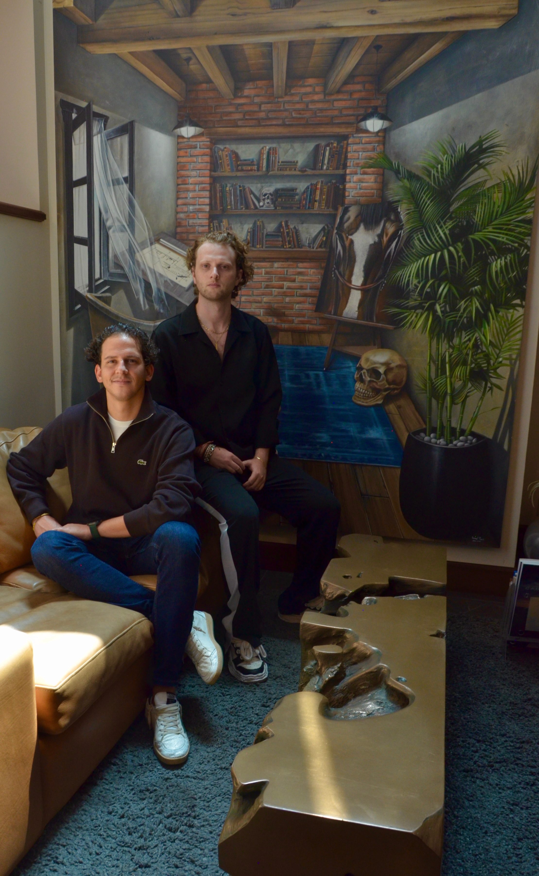 Anthony Salame y Eric Zyman sentados en un interior con arte, libros y mobiliario, fotografía en color